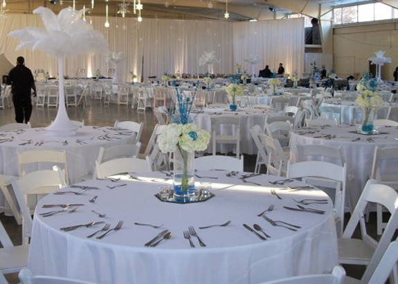 Round tables covered in white tablecloths and white chairs set up in the Agriculture Building for a wedding