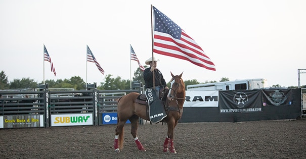 A man sitting on a horse in a dirt arena holding an American flag